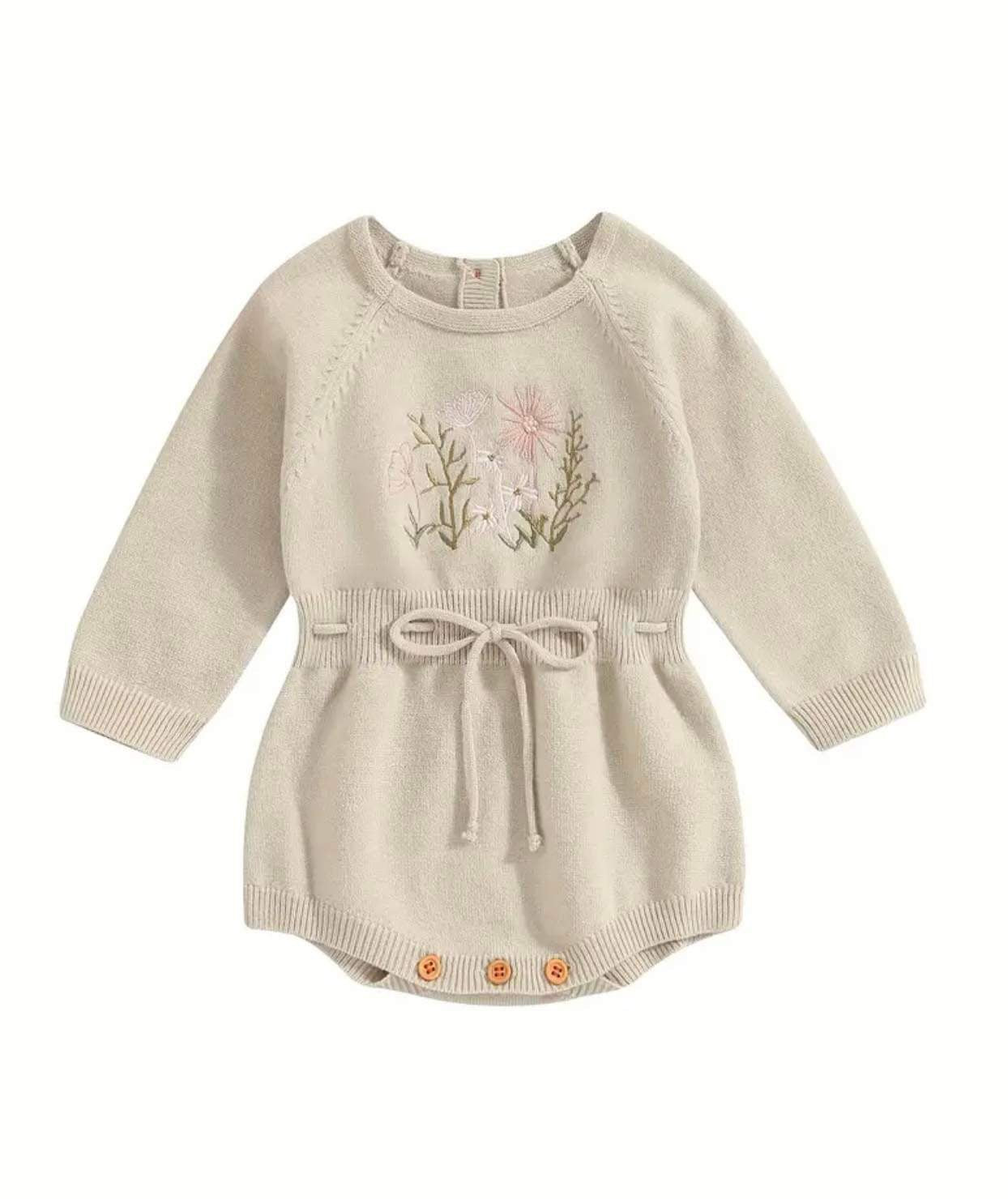 Baby in a knitted floral-embroidered romper with adjustable waist.