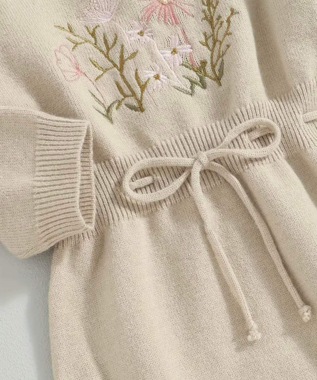 Baby in a knitted floral-embroidered romper with adjustable waist.