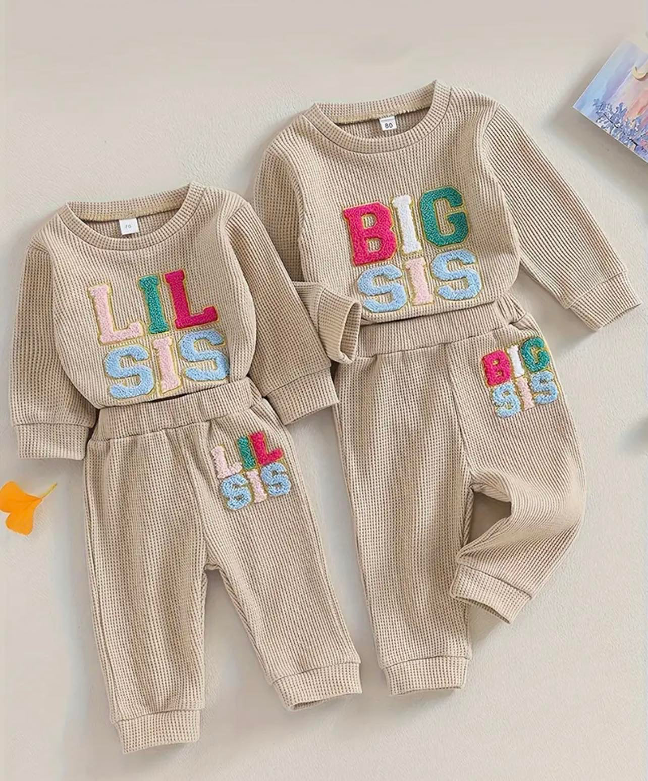 Big Sis and Lil Sis Two Piece Tracksuits side by side, featuring colorful embroidered lettering on cozy waffle knit fabric for baby and toddler girls.