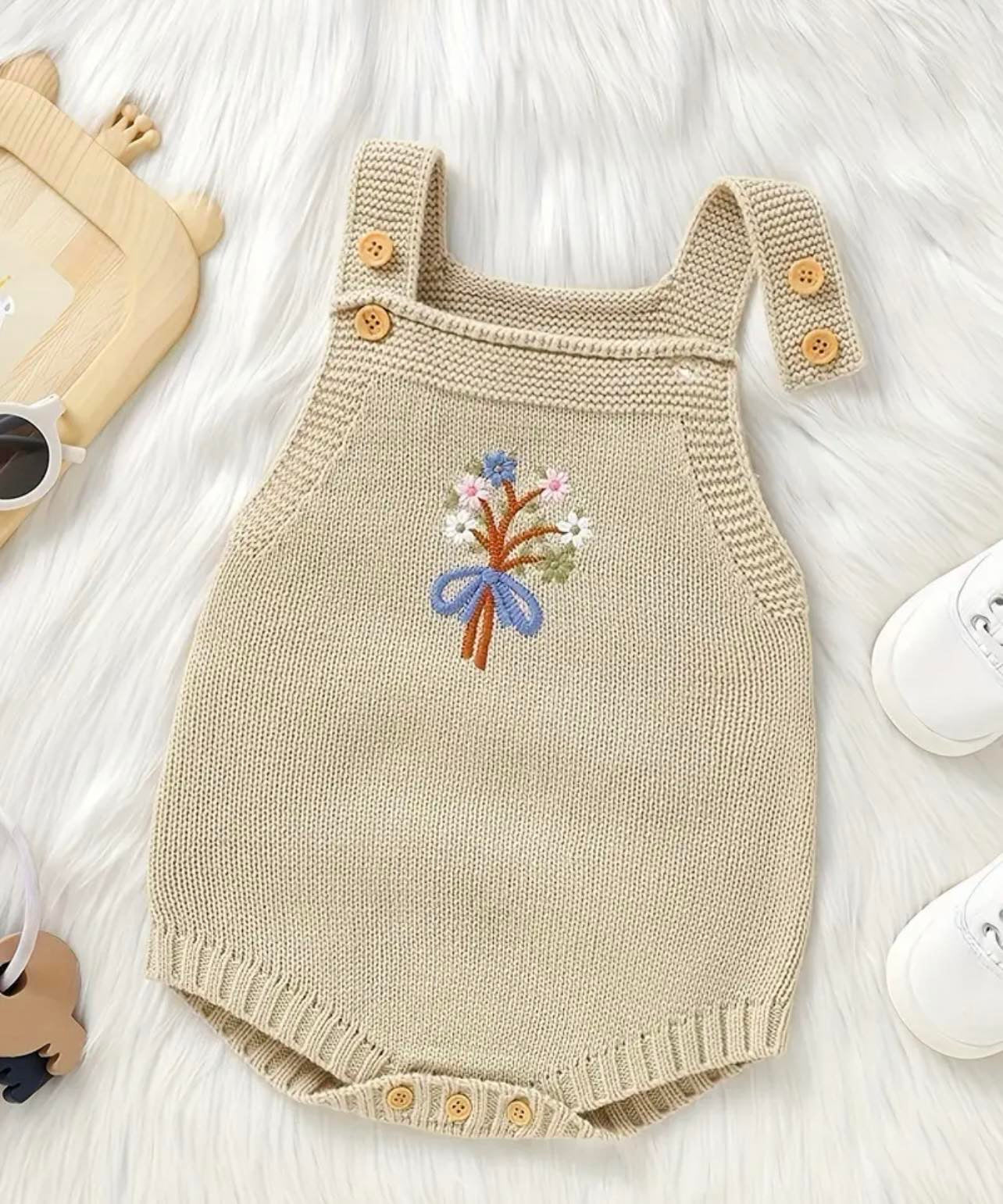 Knitted romper with floral embroidery for babies.