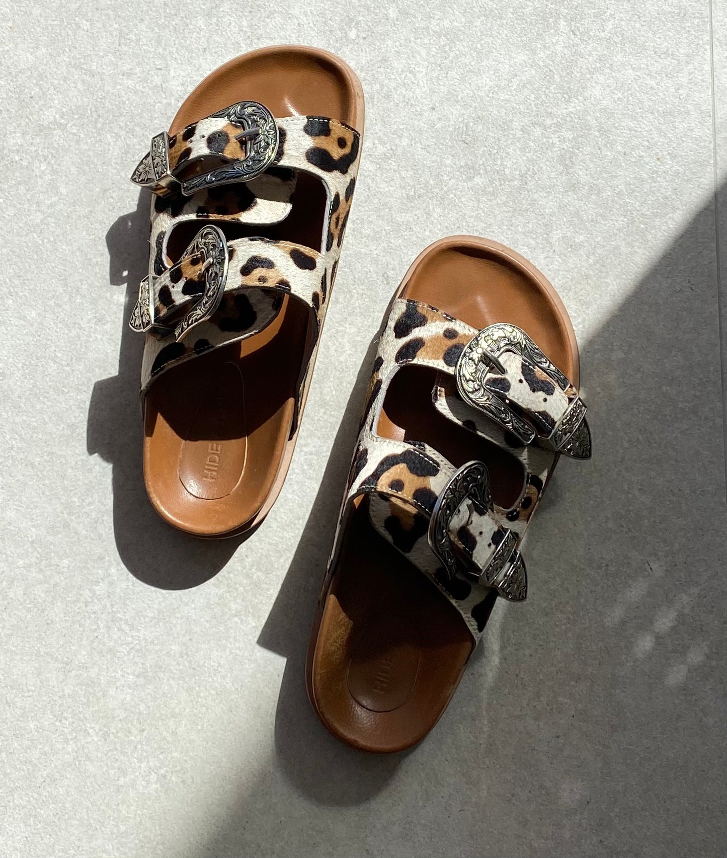 Leopard print luxe sandals with silver buckle detailing and stud accents, offering a unique blend of western style and modern comfort.