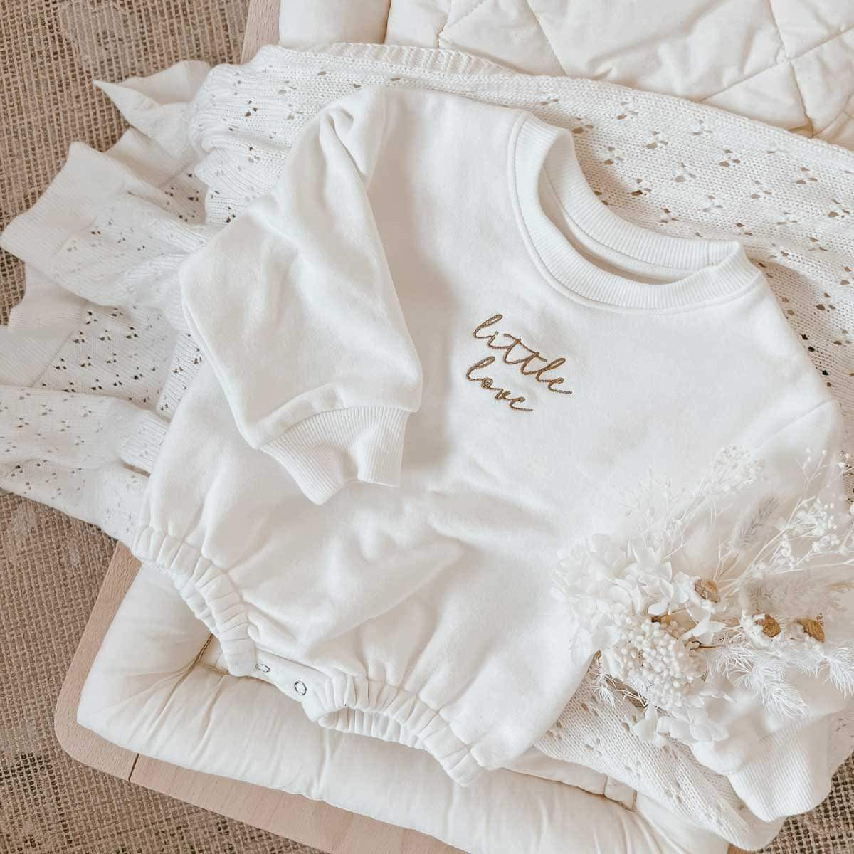 The Little Love Bubble Romper in milk color with bronze embroidery, laid flat to display its soft fleece lining and full sleeve design. Features include an O-neck collar and easy snap button closures, perfect for keeping your baby snug and fashionable.