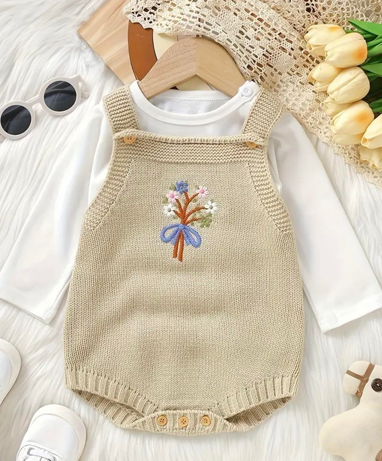 Knitted romper with floral embroidery for babies.