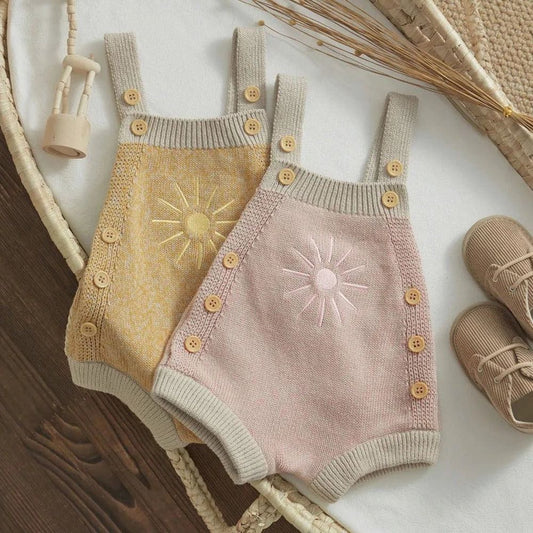 Baby girl in a yellow and pink knitted ribbed romper with sun embroidery and adjustable straps.