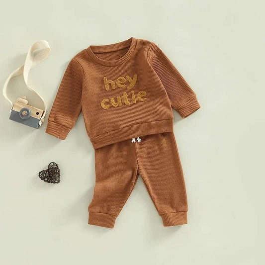 The Hey Cutie Caramel 2-Piece Tracksuit Set featuring a long-sleeve sweatshirt with 'Hey Cutie' print and matching drawstring pants. Made from super-soft waffle fabric, this unisex outfit is perfect for fall and winter, ensuring comfort and style for babies.