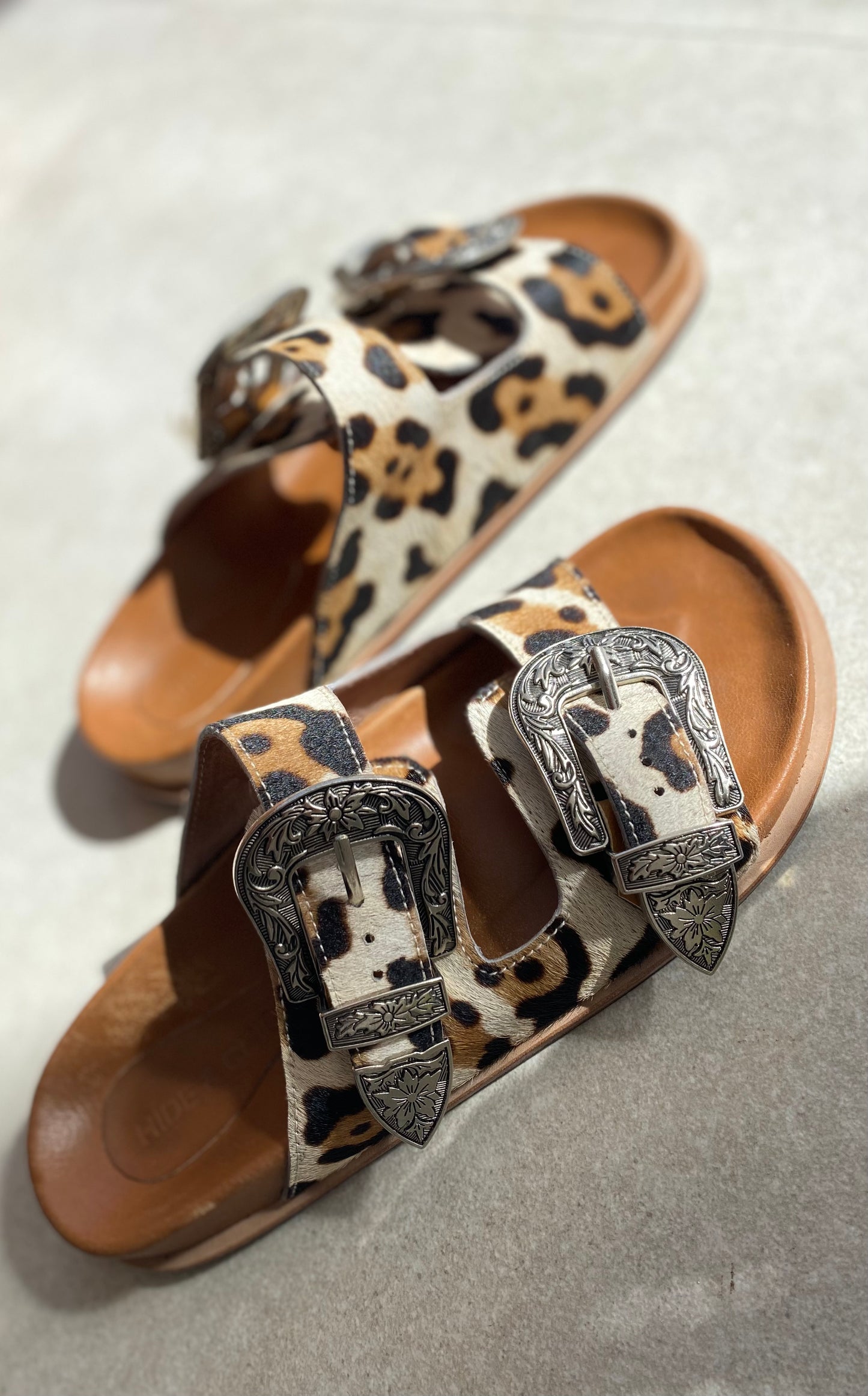 Western-style slide sandals with adjustable straps and a comfortable leather sole, designed with cowboy buckles and silver studs for a trendy look.