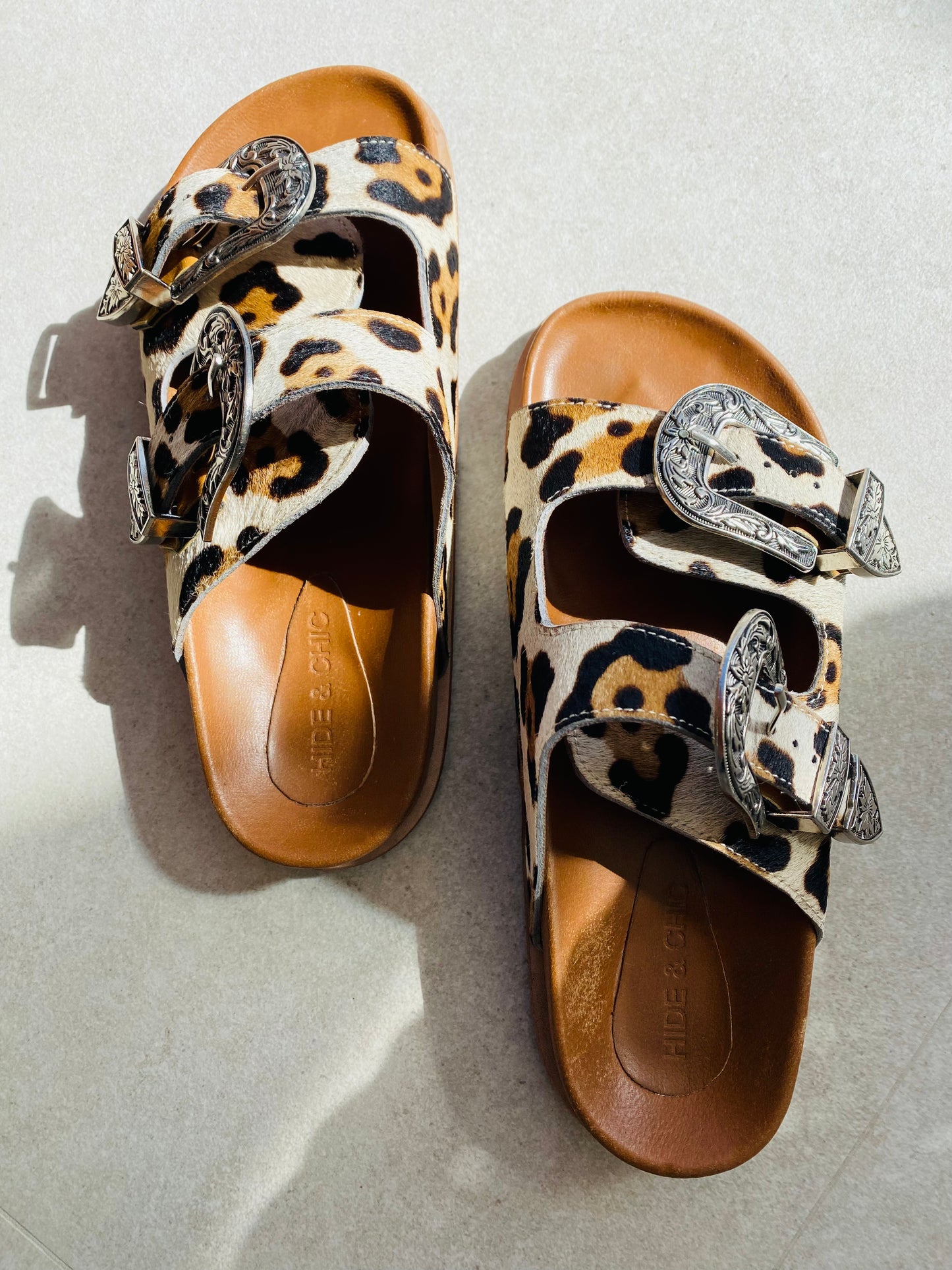 Western-style slide sandals with adjustable straps and a comfortable leather sole, designed with cowboy buckles and silver studs for a trendy look.